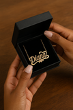 Collier prénom personnalisé Diana doré tenu par des mains féminines manucurées, bijou élégant en acier inoxydable.