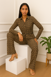 Femme assise avec élégance portant une combinaison chic noire et dorée à motifs géométriques.