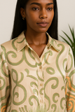 Gros plan sur le haut de l’ensemble en satin beige à motifs verts, chemise boutonnée col classique.