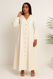 Femme en robe longue boutonnée crème, col en V et boutons dorés, style élégant.