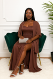 Femme assise en robe bustier marron avec fente et pochette argentée.
