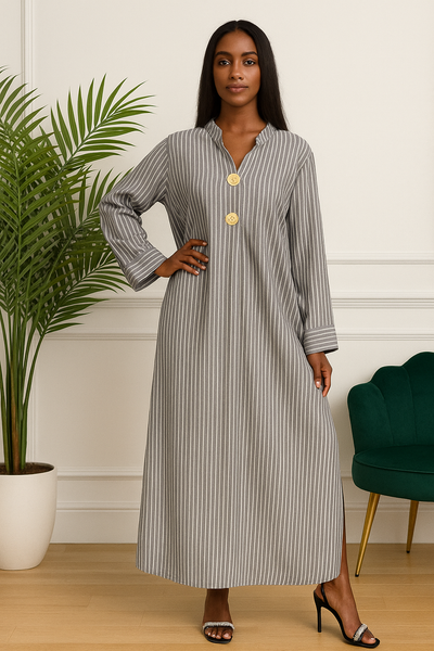 Femme en robe longue rayée grise avec boutons dorés, debout dans un intérieur chic.