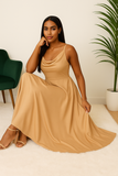 Femme élégante assise portant une robe longue satinée camel, fluide et chic, avec bretelles fines et encolure drapée