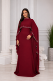 Femme portant une robe de soirée longue bordeaux avec cape et détails scintillants