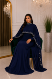 Femme assise portant une robe de soirée longue bleu roi avec cape bordée de détails scintillants, tissu déployé de chaque côté
